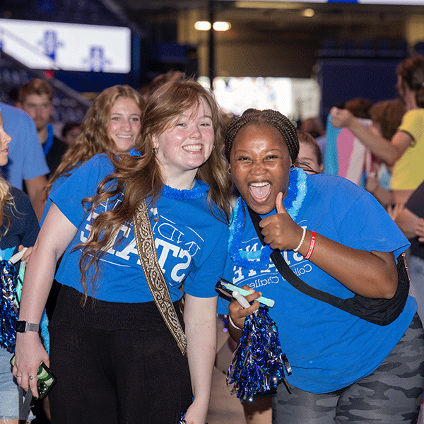 Two female students in blue ISU shirts smile, one is giving a thumbs up